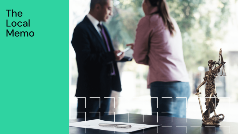 Lawyer and clients having meeting with small bronze statue of lady justice in the forefront on a desk with a pen and piece of paper with green block on the right-hand side and The Local Memo in black text on it, and white traingles in the foreground.png