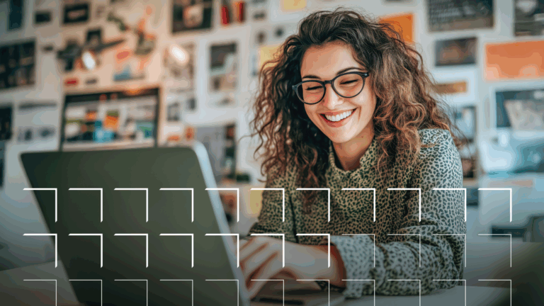 Smiling woman with curly hair and glasses working on a laptop in a creative, colorful office space.