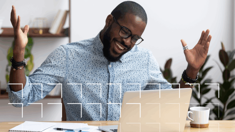 Man at a desk looking very happy with what he sees on the screen of his laptop.